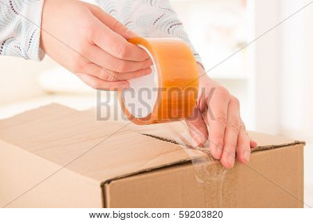 Hands with roll of transparent packaging, adhesive tape on a cardbox