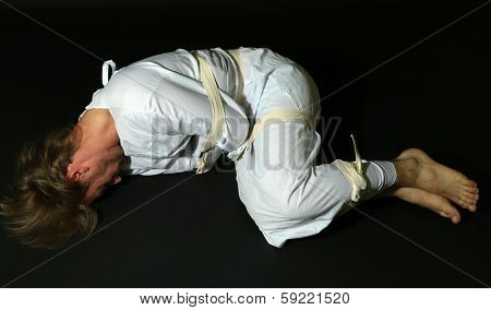 Mentally ill man in strait-jacket on black background