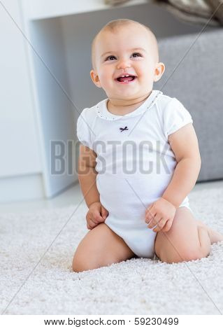 Full length of a cute cheerful baby sitting on carpet at home
