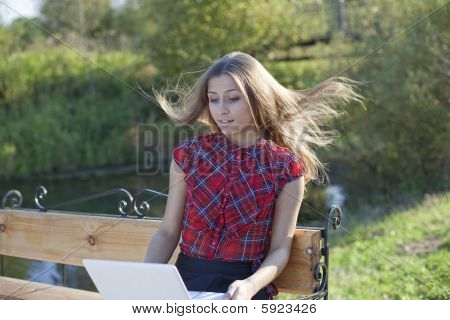 Meisje op Bank met laptop in herfst park-wind blow up haar