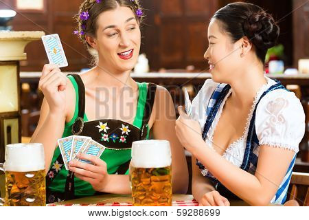 In Pub - friends in Tracht, Dirndl and Lederhosen drinking a fresh beer in Bavaria, Germany playing cards