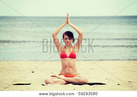 Young woman is sitting on the beach in joga position.