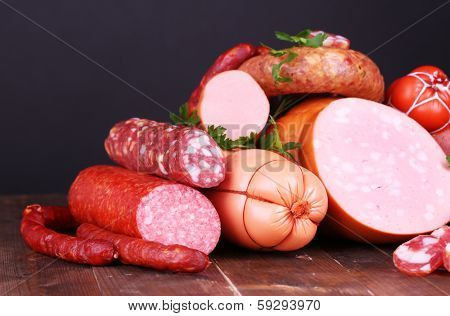 Lot of different sausages on wooden table on black background