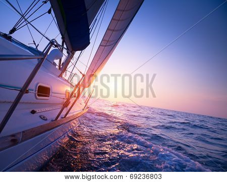 Sail boat gliding in open sea at sunset