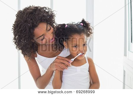 Pretty mother helping her daughter brush her teeth at home in the bathroom
