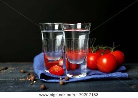 Glasses of ouzo and tomatoes on wooden table, on grey background