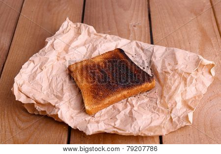Burnt toasted bread on piece of paper and wooden table background