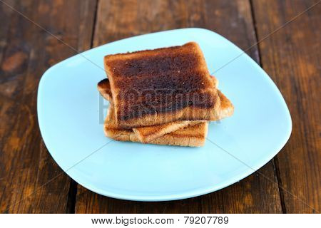 Burnt toast bread on turquoise plate, on wooden table background