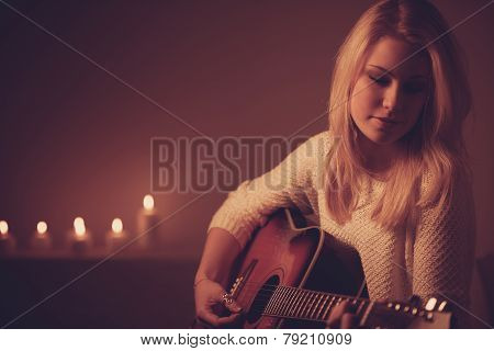 Young Blonde Woman Playing Guitar In Candle Light