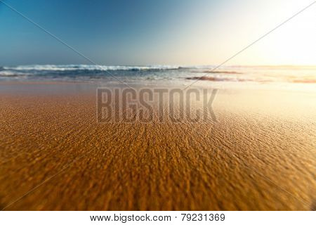 Sandy beach and blue sea with waves at sunset