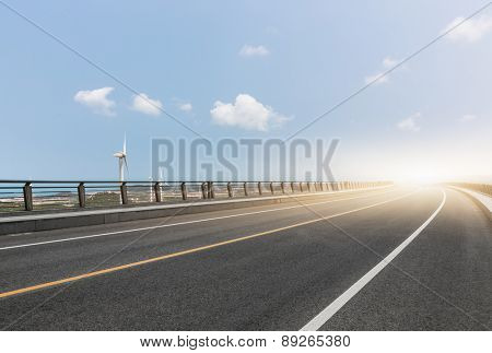 Wind turbines on landscape along empty road against sky.