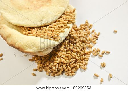 Wheat grains placed over baked flat bread on white background.