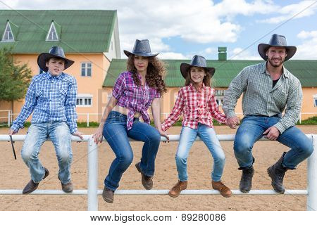 cowboy family sit on the fence of the corral