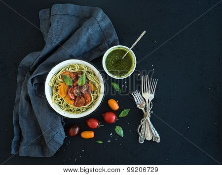 Pasta spaghetti with pesto sauce, basil, slow-roasted cherry-tomatoes in rustic metal bowl on dark g
