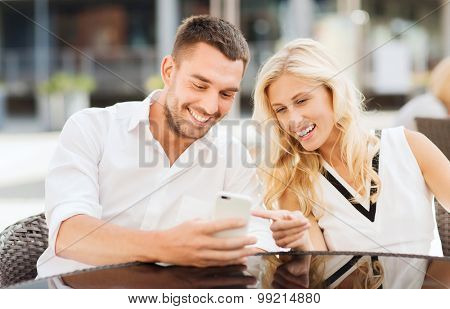 love, date, technology, people and relations concept - smiling happy couple with smatphone at city street cafe