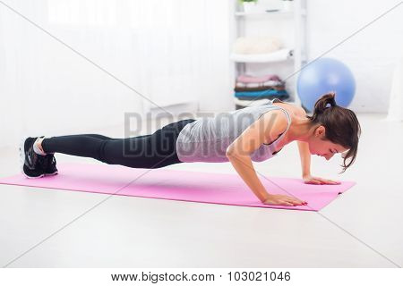 fit woman doing push-ups on the floor in her living room an exercise mat at home