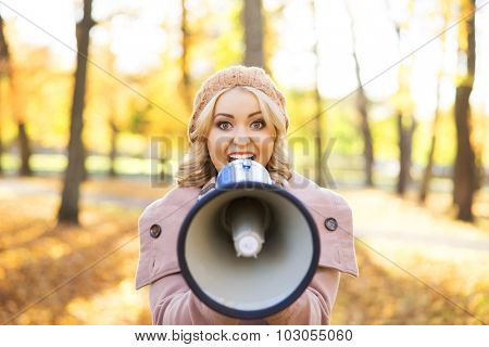 Beauitiful woman speaking to amplifier in the autumn park.