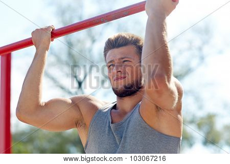 fitness, sport, exercising, training and lifestyle concept - young man doing pull ups on horizontal bar outdoors