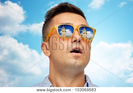 travel, tourism, sightseeing, emotions and people concept - face of man in sunglasses looking at big ben tower over blue sky and clouds background
