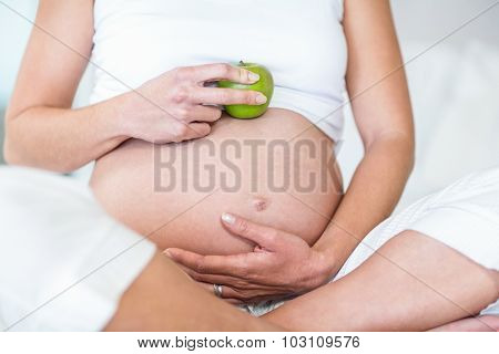 Midsection of pregnant woman with Granny smith on belly sitting in bedroom