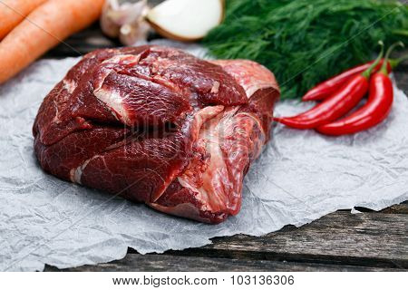 Raw Ox Cheek On Crumpled Paper,  Decorated With Greens And Vegetables. On Old  Wooden Table