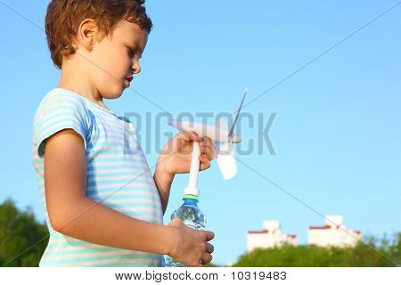 Kleiner Junge gegen blauen Himmel spielt mit windbetriebenen Generator