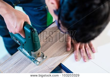 DIY worker cutting wooden panel with jig saw