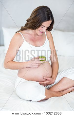 Happy woman with Granny Smith on belly sitting in bedroom