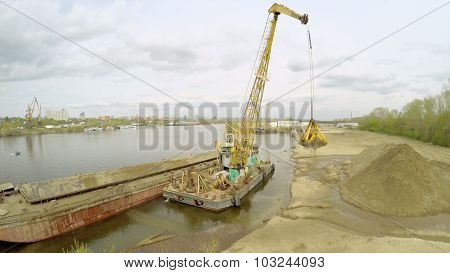SAMARA - MAY 10, 2015: Crane unloads sand from barge on shore of Volga river at spring cloudy day. Aerial view video frame