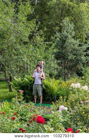 Little Girl Sitting On The Daddy Shoulders Among Flowers