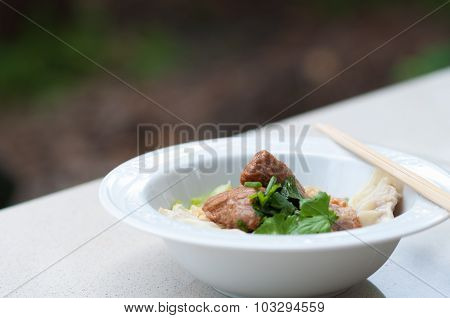 Egg noodle with delicious stewed pork and dumpling in white bowl.