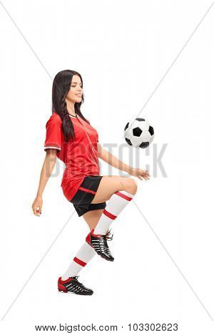 Full length profile shot of a female soccer player juggling a ball on her knee isolated on white background