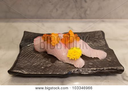 Kampachi sushi with Uni and Ikura on top on black ceramic plate