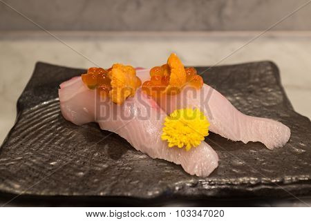 Kampachi sushi with Uni and Ikura on top on black ceramic plate