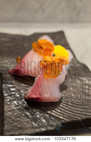 Kampachi sushi with Uni and Ikura on top on black ceramic plate