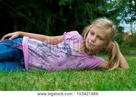 Small Blonde Girl Child With Ponytail Lay Aside In Grass Smiling Happy