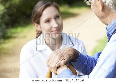 Senior Man's Hands Resting On Walking Stick With Care Worker In Background