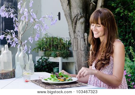 Pretty woman eating healthy green salad outdoors in garden, relaxed and happy in alfresco dining