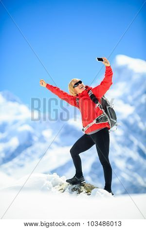 Young happy woman hiker doing smartphone selfie self-portrait on mountain peak summit in winter moun