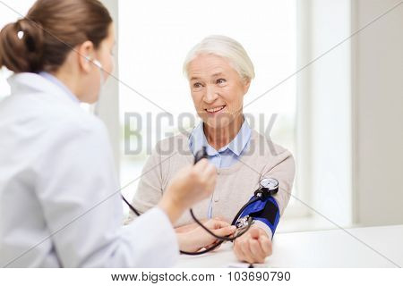medicine, age, health care and people concept - doctor with tonometer checking happy senior woman blood pressure level at hospital