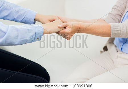 people, age, family, care and support concept - close up of senior and young woman  holding hands