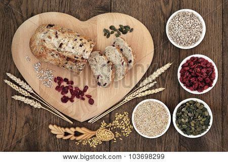 Cranberry seed bread on heart shaped board with wheat and sheaths, sunflower and pumpkin seeds, oatmeal  and dried cranberries over old oak background.