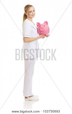 Young beautiful female doctor holding a piggybank.