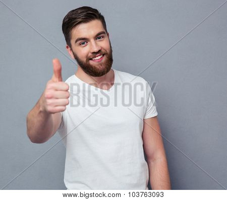 Portrait of a smiling casual man showing thumb up and loking at camera over gray background