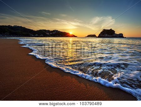Rolling waves against the smooth sand and sunset peaking through the hill