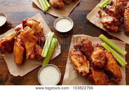different flavored chicken wings with ranch dipping sauce and celery sticks on wooden table