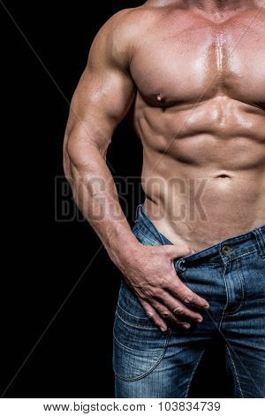 Midsection of sexy man pulling denim while standing against black backrgound