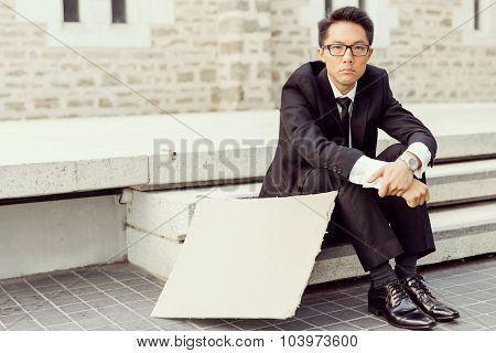 Businessman in a city street hsitting next to blank banner