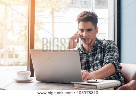 Businessman Using Mobile Phone While Lookingat Laptop On Wooden Table In Coffee Shop