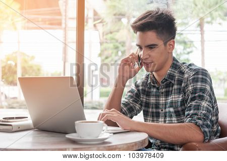 Businessman Using Mobile Phone While Lookingat Laptop On Wooden Table In Coffee Shop